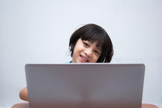 Cute smart Asian boy is happily using his laptop to study online by himself at home Online learning conceptSelfStudy