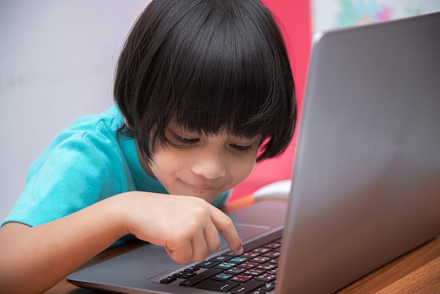 Cute smart Asian boy is happily using his laptop to study online by himself at home Online learning conceptSelfStudy