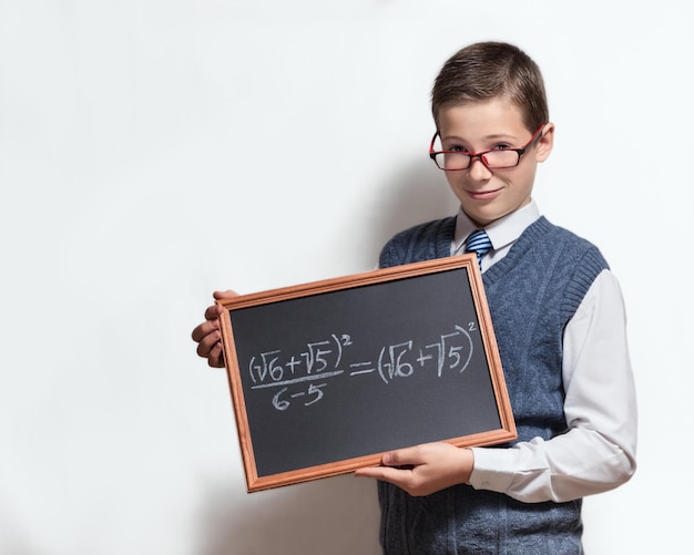 Cute smart schoolboy teenager in a glasses shows the black chalkboard with the mathematical equation