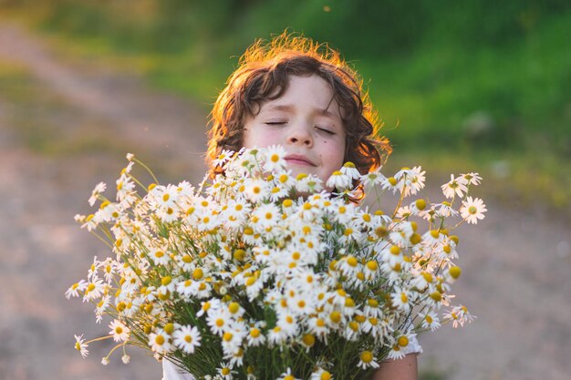 Cute smiling boy at camomile field at sunset in soft sunlight Life without allergies breathe freely Boy and daisies Child dreaming and smiling against the background of a camomile field