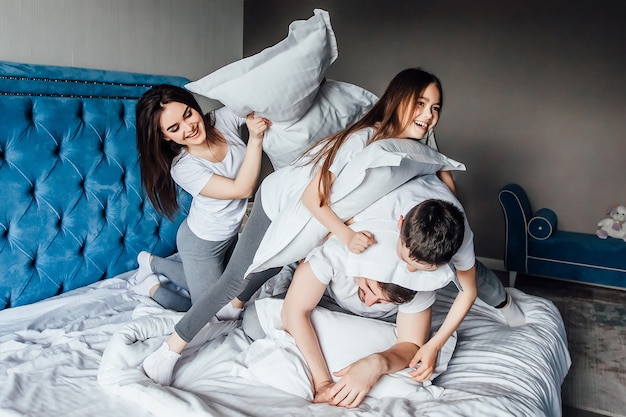 Cute smiling family fighting with pillows on bed in bedroom.