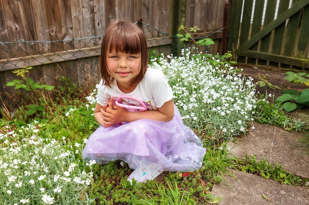 A cute smiling girl is playing in the backyard with small pink bag Sunny day