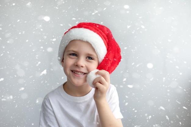 Cute smiling happy little boy in a Christmas red cap. Light snow background. Concept Christmas, New Year atmosphere.