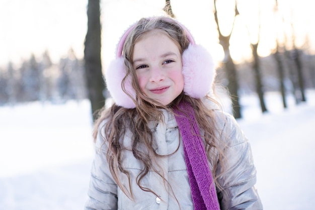 Cute smiling kid girl wear scarf and fluffy headphones over sunny light