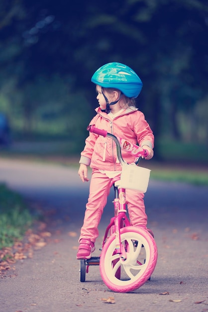 Cute smiling little girl with bicycle and helmet on road in the park