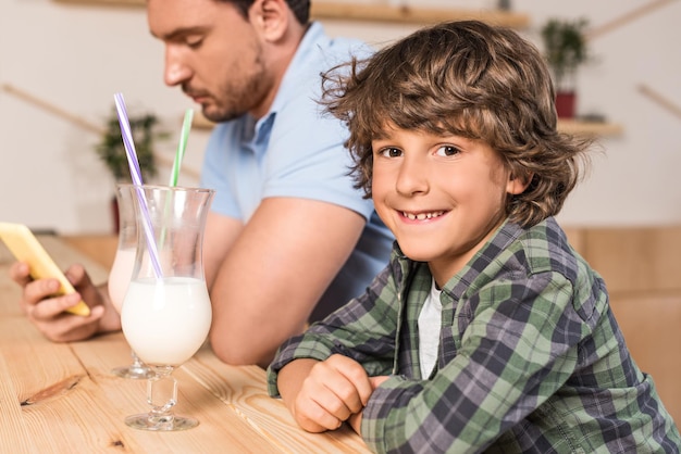 Cute smiling son and his father drinking milkshakes in cafe