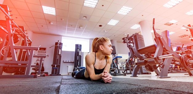 Cute sporty fitness model rests on floor in modern gym Beautiful trained woman with perfect body