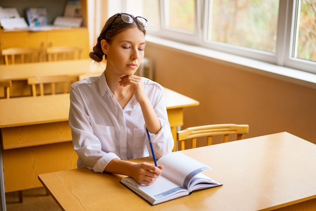 Cute student sitting with a notebook at the Desk by the window, thoughtful view