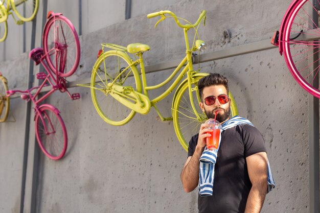 Cute stylish arab young male hipster with a mustache and a beard and wearing glasses drinking juice