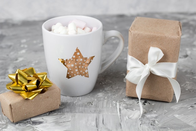 Cute stylish cup with marshmallows and gift box concrete gray background