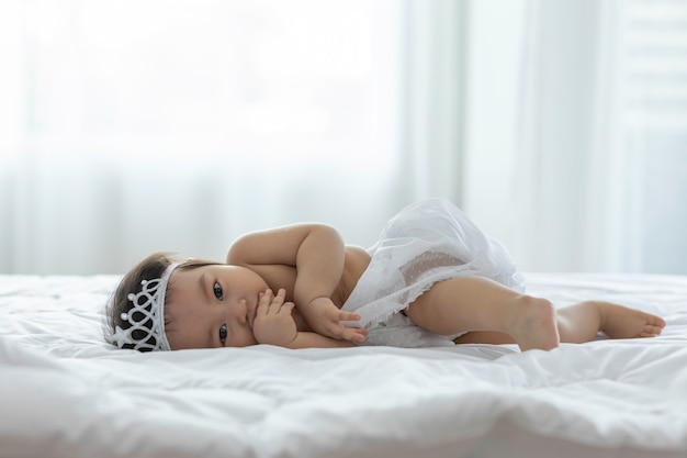 Cute Sweet Adorable Asian Baby wearing bride dress and diadem Sitting on white bed smiling and playing with happiness emotional in cozy bedroom,Healthy Baby Concept