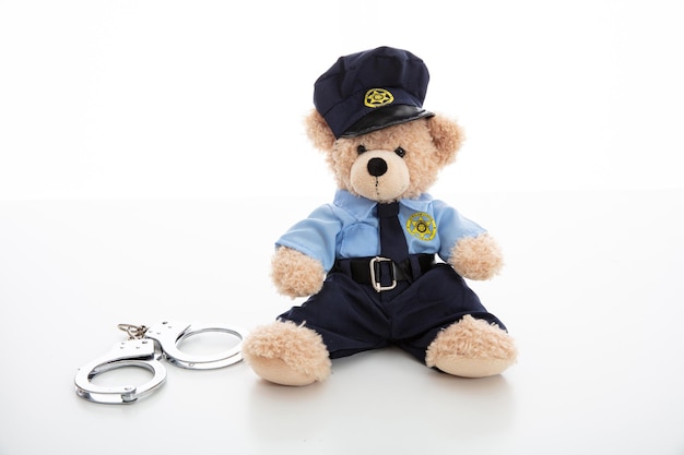 Cute teddy in policeman uniform and handcuffs isolated against white background