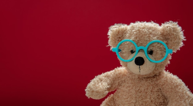 Cute teddy wearing eyeglasses against red background