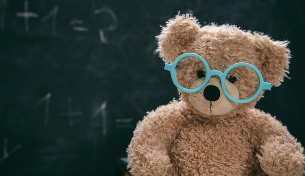 Cute teddy wearing glasses against empty blackboard