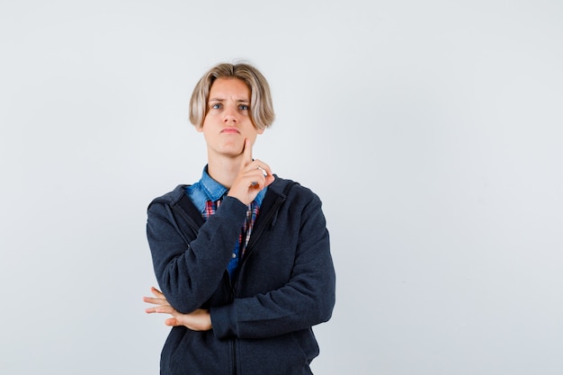 Cute teen boy pondering the matter while looking up in shirt, hoodie and looking hesitative. front view.