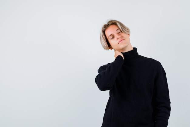 Cute teen boy in turtleneck sweater keeping hand on neck