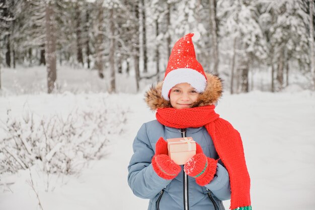 Cute teen girl opens gift box christmas present outdoor in winter child in scarf mittens and santa hat