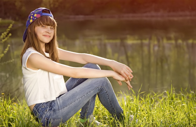 Cute teen girl sits on a grass near lake