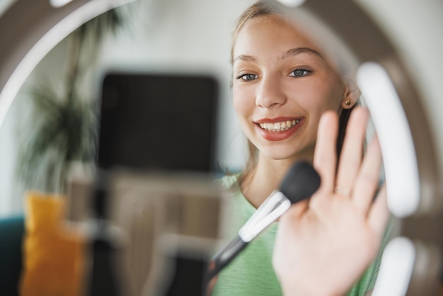 A cute teen girl vlogger live broadcasting make up tutorial to her followers via smart phone at her home.