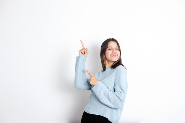 Cute teenage girl brunette on a white background points her fingers up. A place for text. advertisement. High quality photo