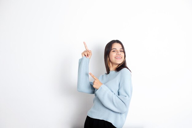 Cute teenage girl brunette on a white background points her fingers up A place for text advertisement