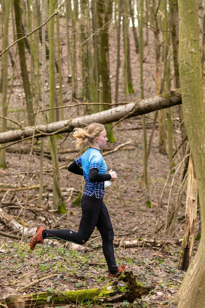 Cute teenage girl wearing sportswear running through a forest during exercise in outdoor orienteering