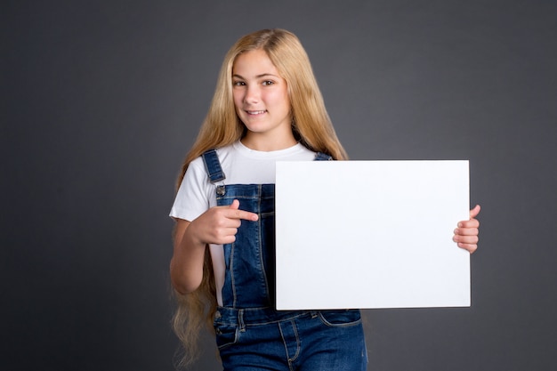 Cute teenage girl with long blond hair holding white blank poster on gray background.