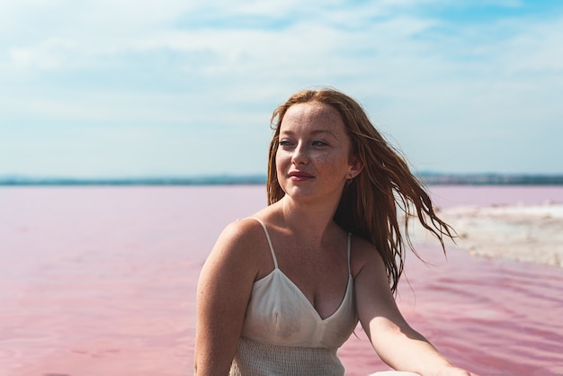 Cute teenager woman wearing white dress sitting on an amazing pink lake