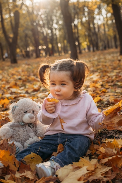 Cute toddler baby girl with soft toy playing outdoors in fall park little girl in the autumn park