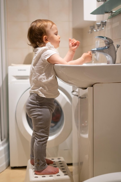 Cute toddler in the bathroom mirror learning how to wash his face