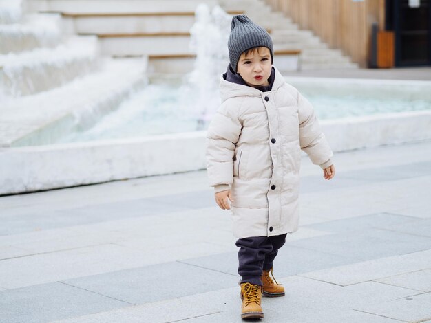 Photo cute toddler boy in fashionable casual warm clothes playing in playground near shopping mall