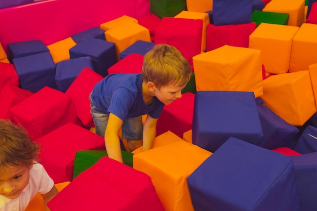 The cute toddler boy is standing among soft cubes