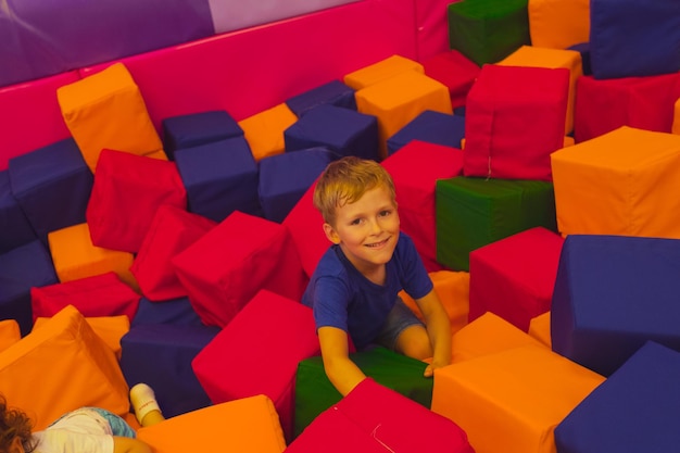 The cute toddler boy is standing among soft cubes