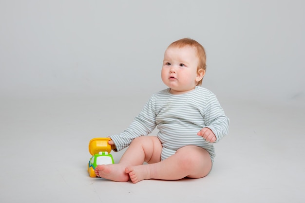 Cute toddler boy old in white bodysuit plays with car toy sitting on a white background space for te