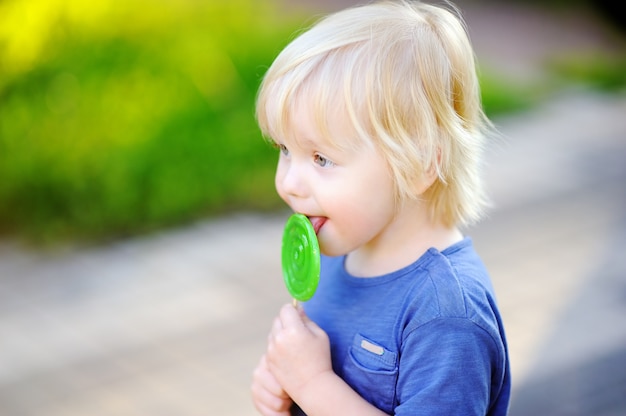 Cute toddler boy with big green lollipop. Child eating sweet candy bar. Sweets for young kids. Summer outdoor fun