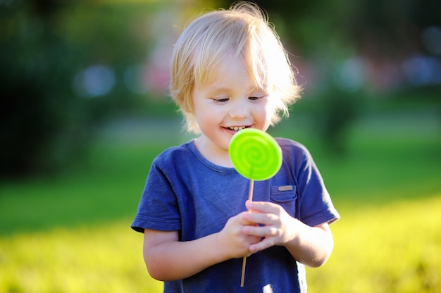 Cute toddler boy with big green lollipop. Child eating sweet candy bar. 