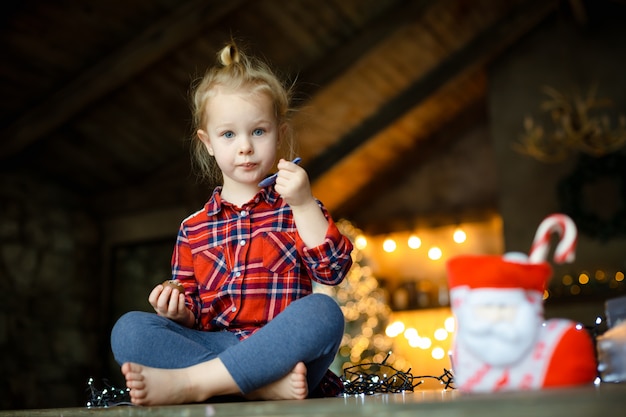 Cute toddler girl eating chocolate egg sitting in a hunting house decorated for Christmas. 