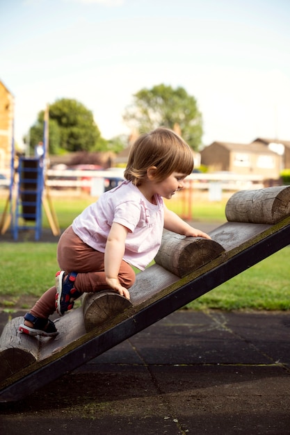 Cute toddler girl at a playground, climbing on the wooden stairs. Education and parenting concept