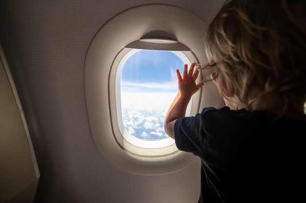 Cute toddler points his finger at the sky through the window first flight concept traveling with