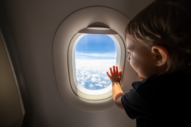 Cute toddler points his finger at the sky through the window first flight concept traveling with