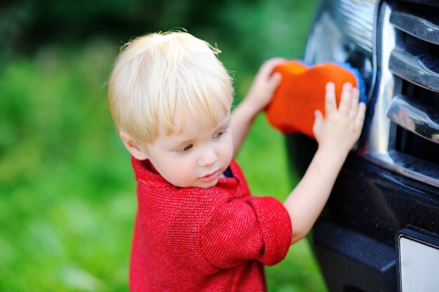 Cute toddler son playing washing fathers's car outdoors