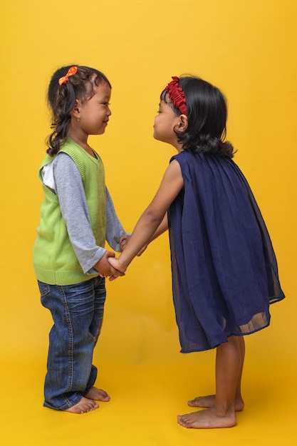 cute two little Asian girl holding hand and looking at each other on yellow background