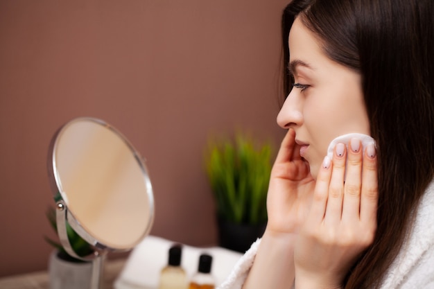 Cute woman in bathroom doing cosmetic procedure for facial skin care