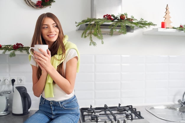 Cute woman drinking coffee near christmas decoration at home