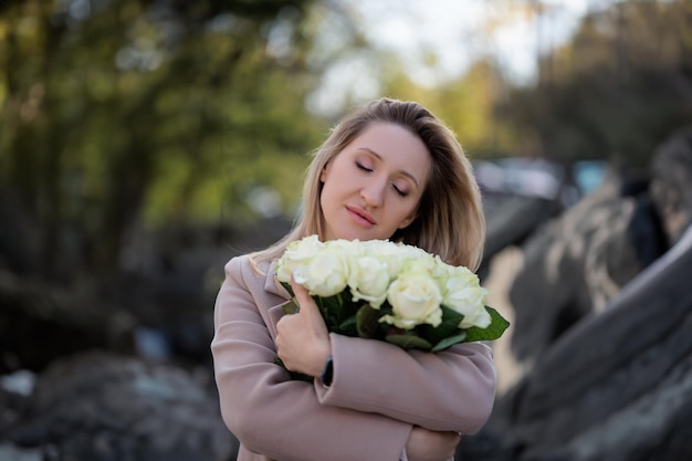 Cute woman hugging a bouquet of white roses with her eyes closed