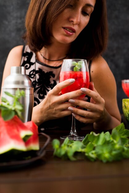 Cute woman is holding watermelon cocktail on dark background