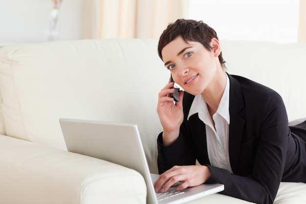 Cute Woman lying on a sofa with a laptop and a phone