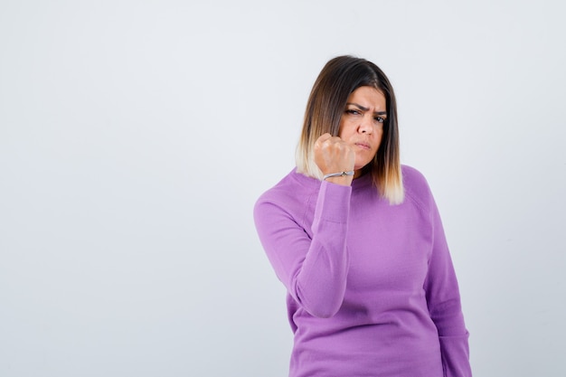 Cute woman showing clenched fist in purple sweater and looking spiteful. front view.