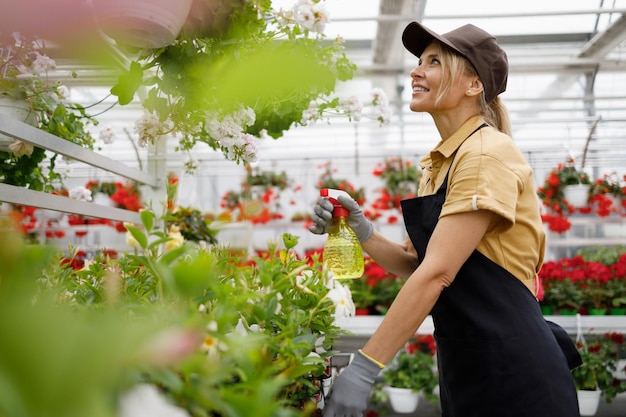 Cute woman spraying flowers with spray bottle in greenhouse