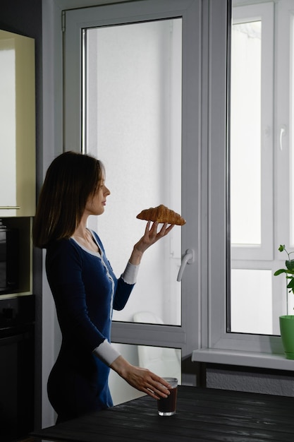 Cute woman standing by the window with croissant in hand